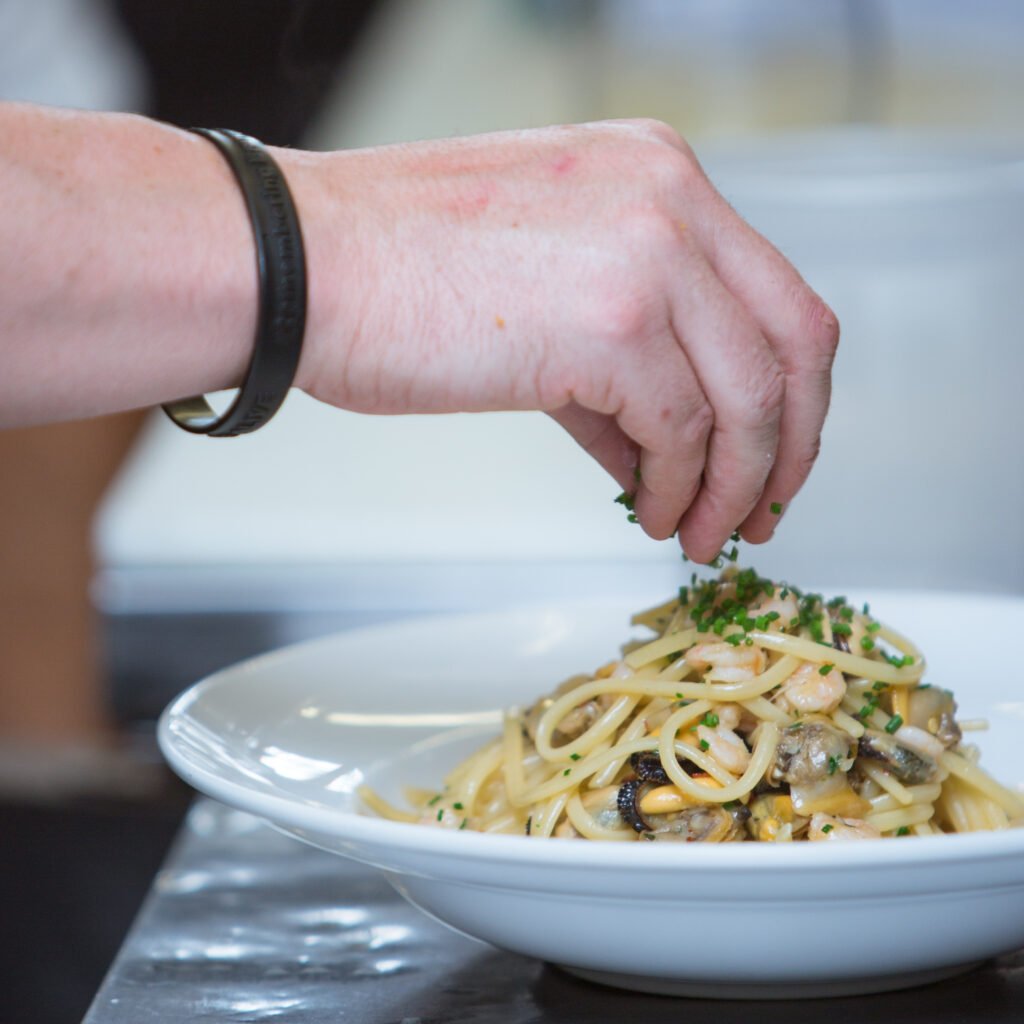 chef adds some greens to pasta with shrimps and mushrooms