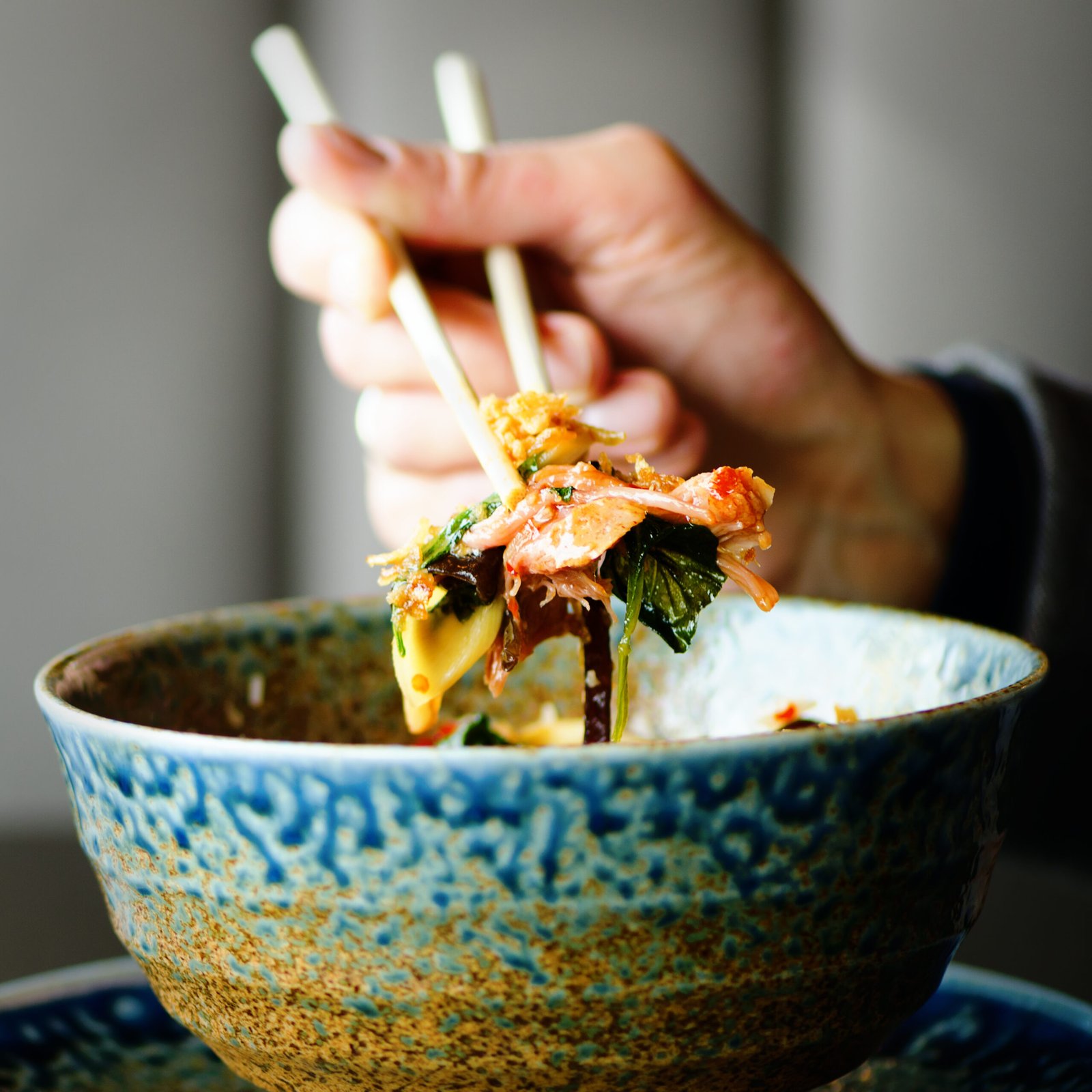 man's hand holding chopsticks over a plate of japanese, thai, chinese meal rice, mushroom, vegetables. cafe, restaurant. business lunch. copy space.